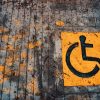 Yellow wheelchair accessibility sign painted on urban pavement with leaves.