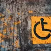 Yellow wheelchair accessibility sign painted on urban pavement with leaves.