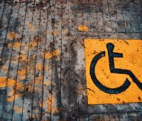 Yellow wheelchair accessibility sign painted on urban pavement with leaves.