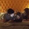 A family enjoying quality time together using a tablet in bed, enhanced by a warm cozy setting.