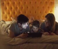 A family enjoying quality time together using a tablet in bed, enhanced by a warm cozy setting.