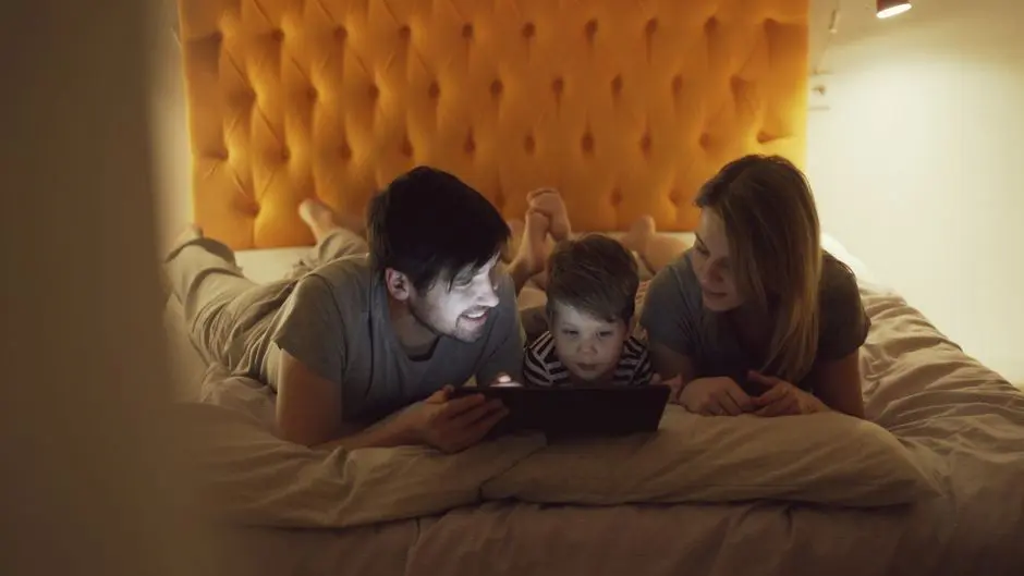 A family enjoying quality time together using a tablet in bed, enhanced by a warm cozy setting.