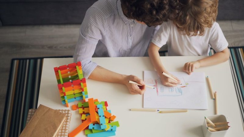 A mother and child drawing with colored pencils at a table, fostering creativity and learning.
