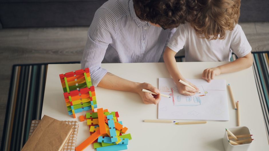 A mother and child drawing with colored pencils at a table, fostering creativity and learning.
