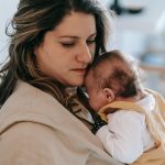 A mother gently holding her baby in a comforting embrace inside a cozy home setting.
