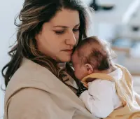 A mother gently holding her baby in a comforting embrace inside a cozy home setting.