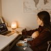 A mother working on a laptop while holding her sleeping baby, creating a warm at-home atmosphere.