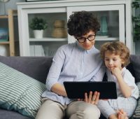 a woman and a child sitting on a couch looking at a laptop