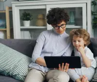 a woman and a child sitting on a couch looking at a laptop