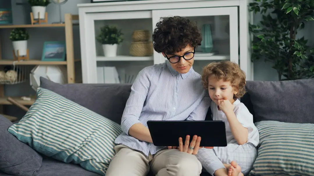 a woman and a child sitting on a couch looking at a laptop